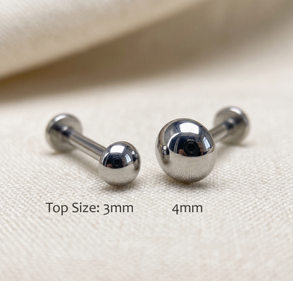 Two silver barbell earrings on a beige fabric background with size labels.