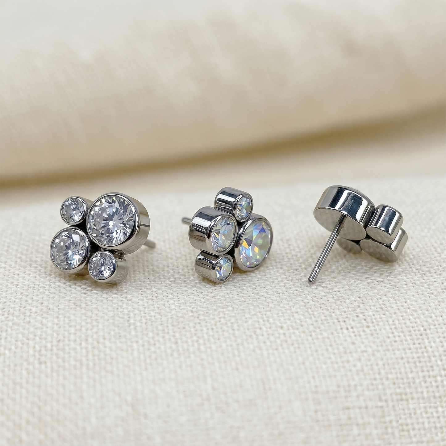 Silver stud earrings with clear gemstones on a beige fabric background