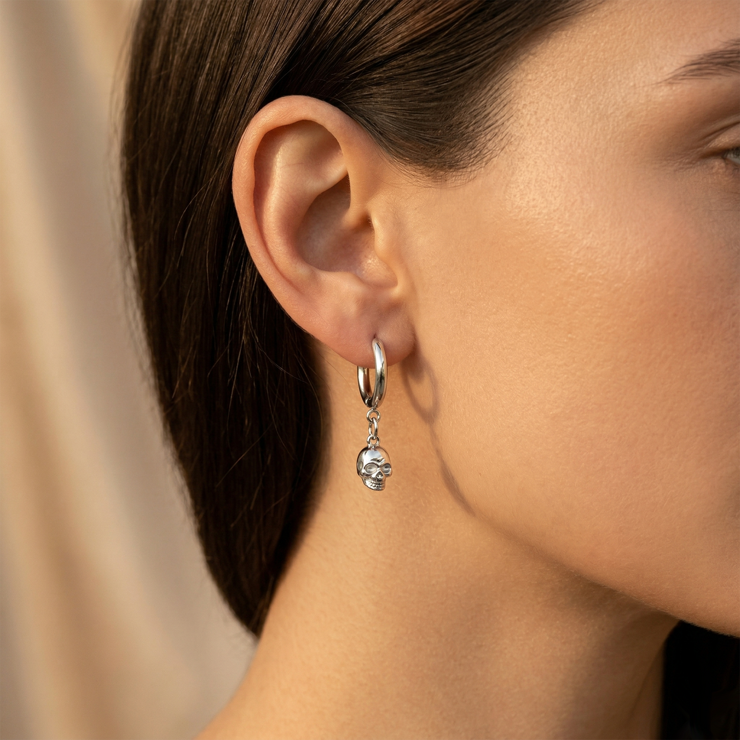 Silver surgical steel skull dangle hoop earring shown on ear close up