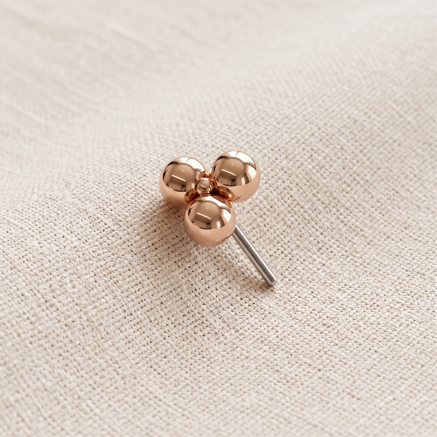 Rose gold clover-shaped earring on a beige fabric background