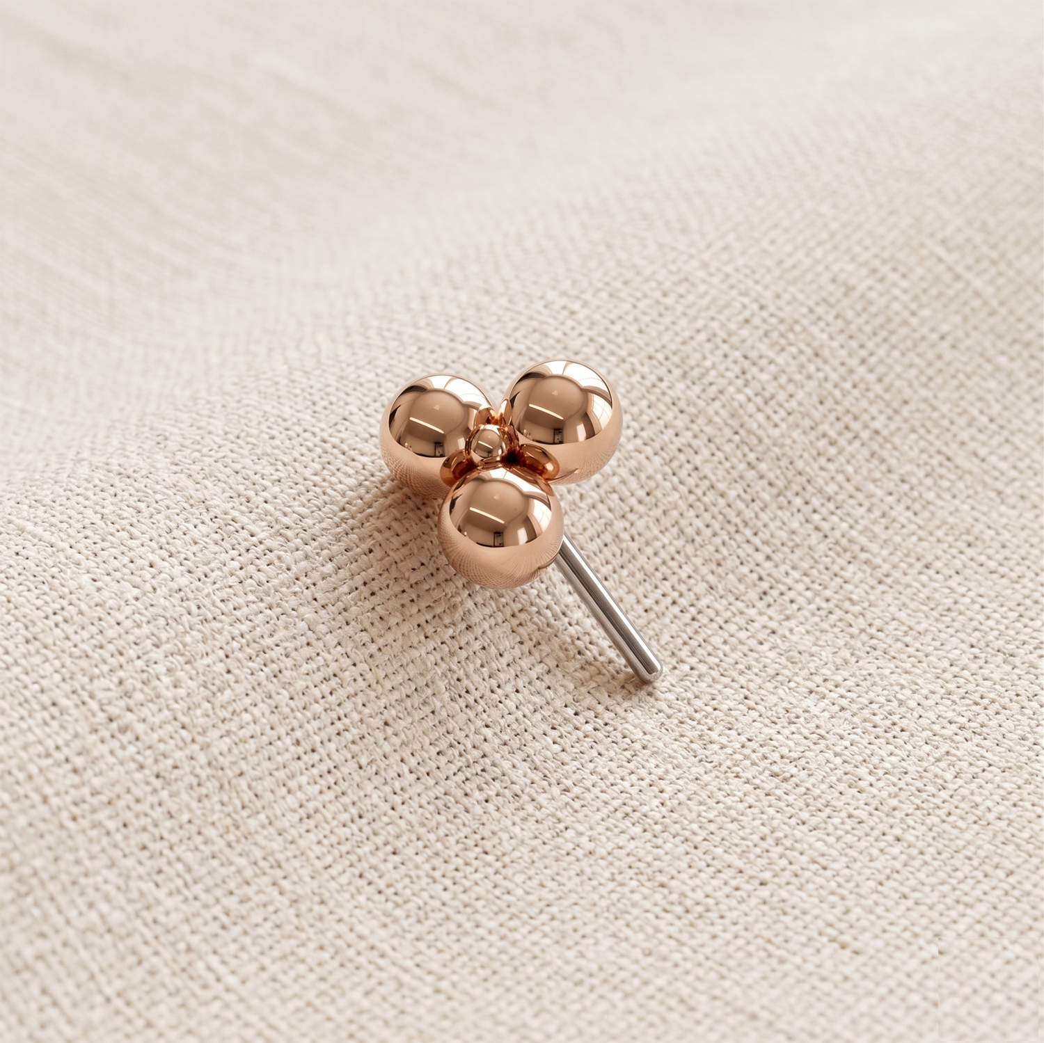 Rose gold clover-shaped earring on a beige fabric background