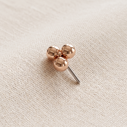 Rose gold clover-shaped earring on a beige fabric background