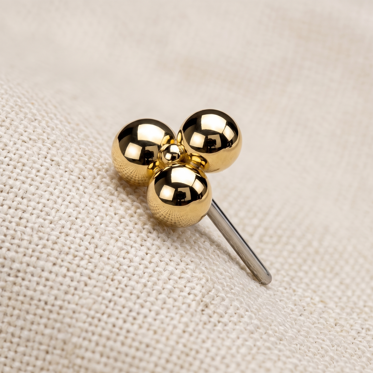 Gold three-ball stud earring on a beige fabric background