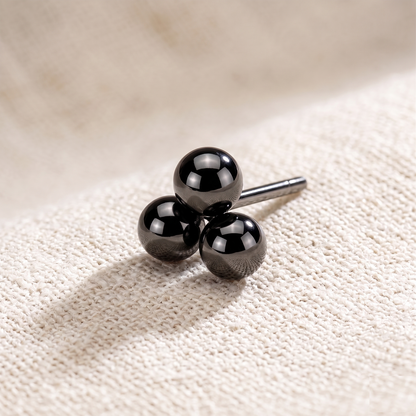 Black three-ball stud earring on a textured beige surface