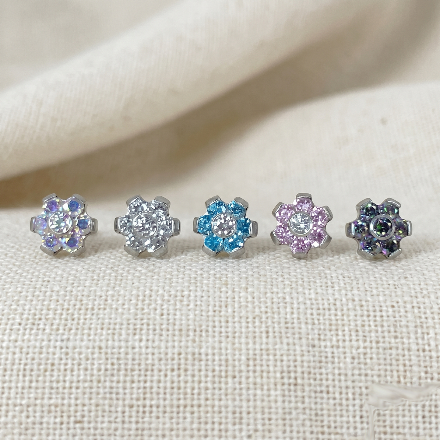 Set of five floral stud earrings with multicolored gemstones on a beige fabric background