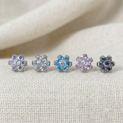 Set of five floral stud earrings with multicolored gemstones on a beige fabric background