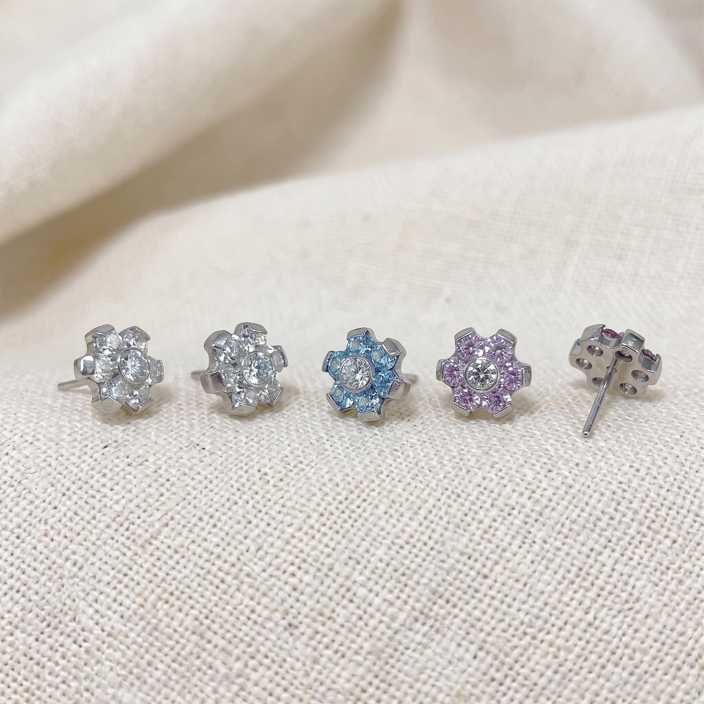 Set of five floral stud earrings with colored gemstones on a beige fabric background