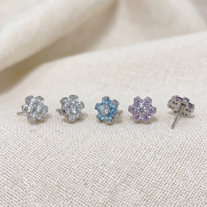Set of five floral stud earrings with colored gemstones on a beige fabric background