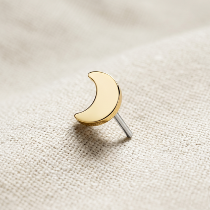 Gold crescent moon earring on a textured beige background