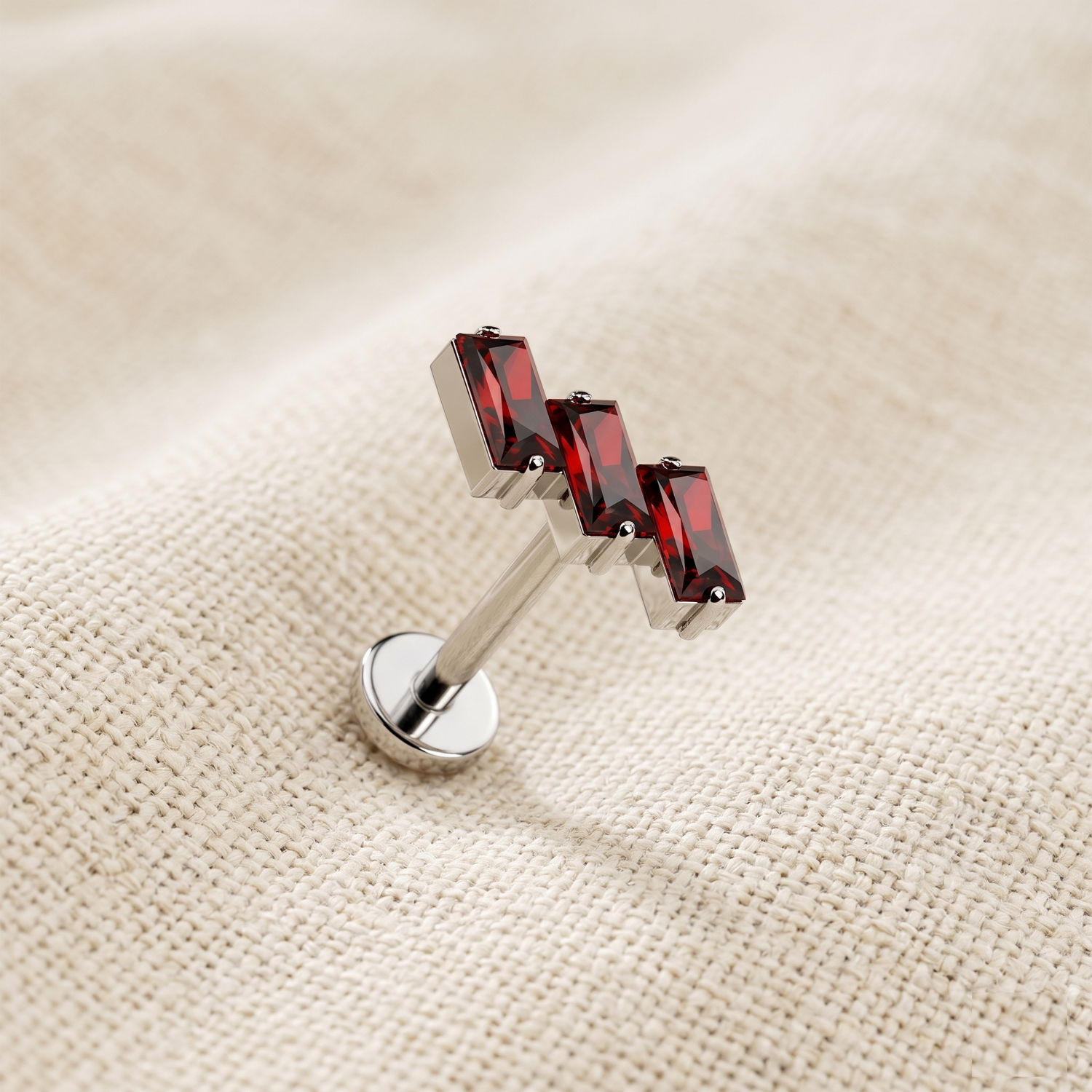 Silver lip ring with red gemstones on a beige fabric background