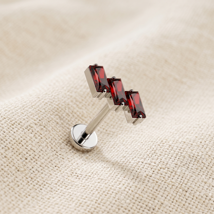 Silver lip ring with red gemstones on a beige fabric background