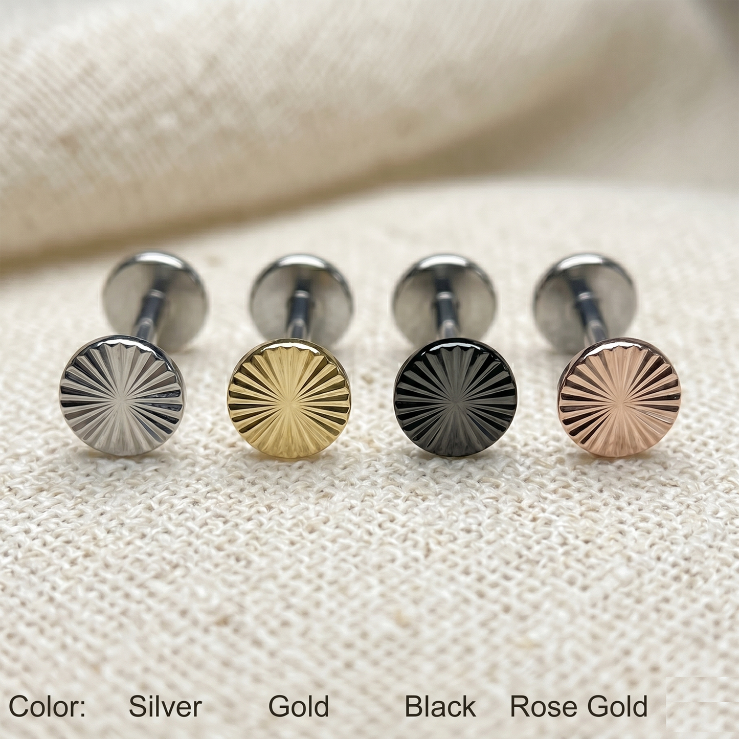 Set of round metal studs in silver, gold, black, and rose gold on a textured beige surface.