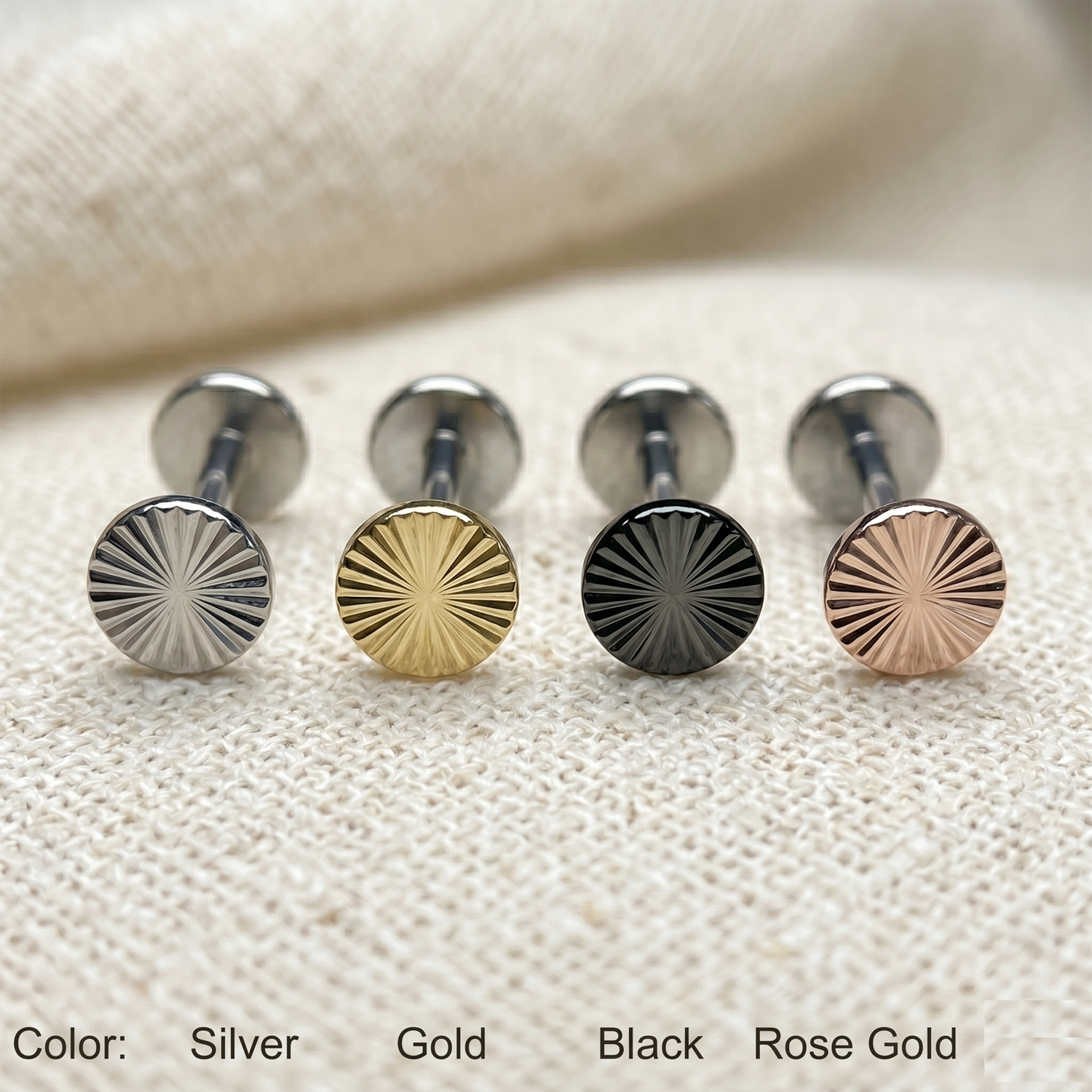 Set of round metal studs in silver, gold, black, and rose gold on a textured beige surface.