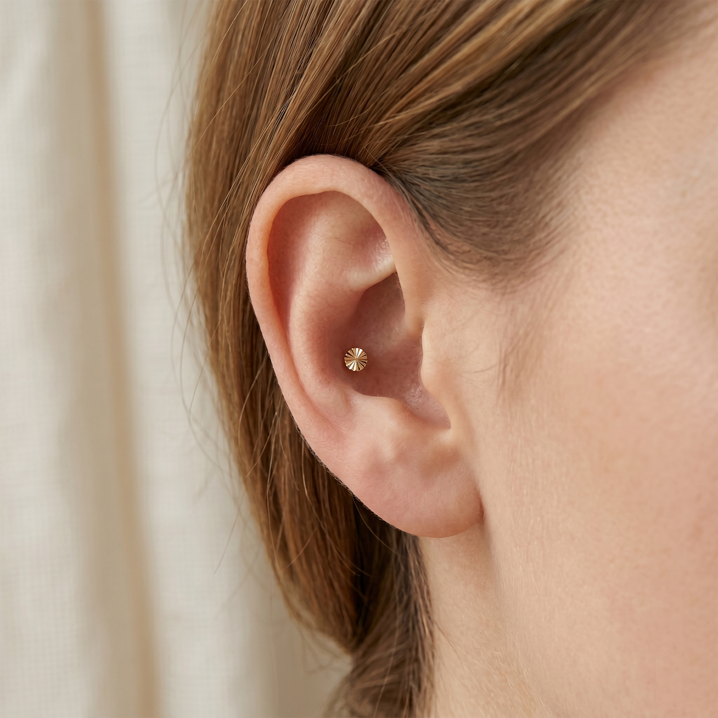 Close-up of an ear wearing a gold stud earring with a neutral background
