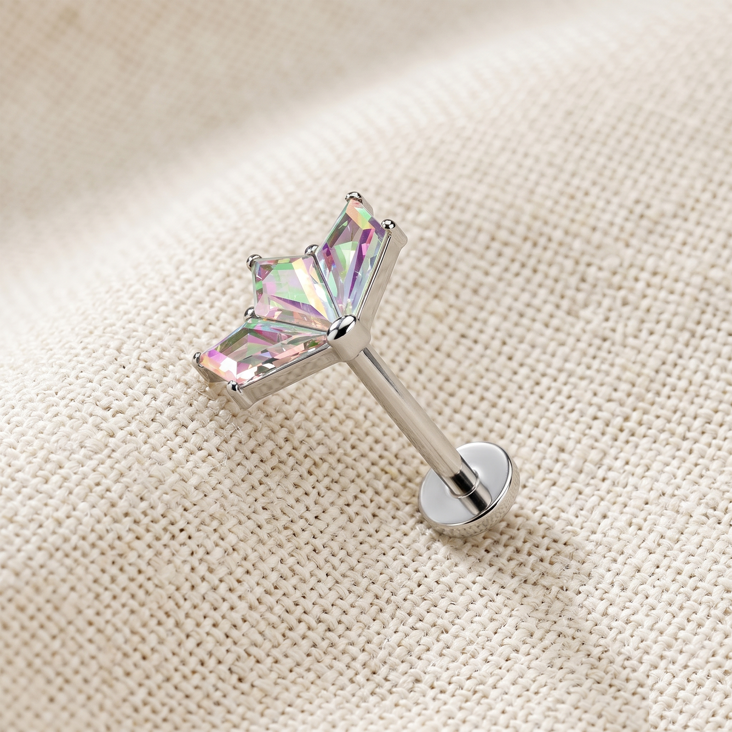 Silver stud earring with a colorful gemstone on a beige fabric background