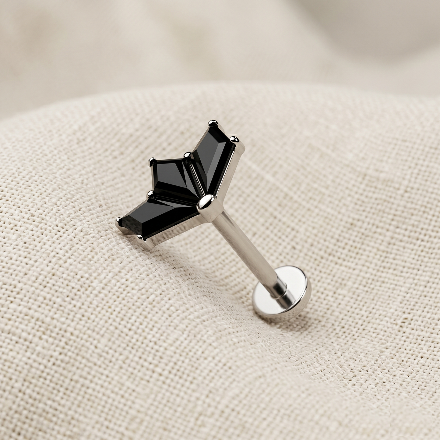 Silver lip ring with black gemstone on a beige fabric background