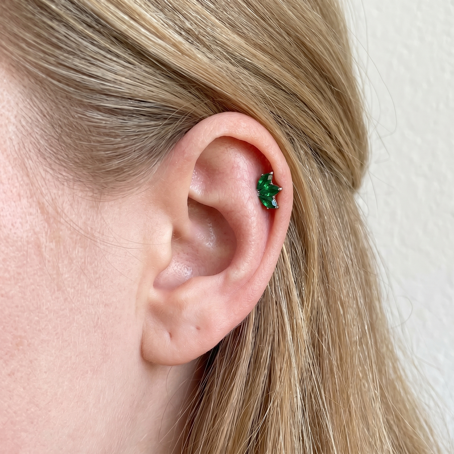 Close-up of an ear wearing a green earring with blonde hair.