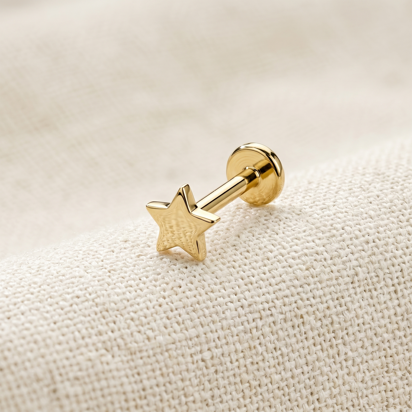 Gold star-shaped earring on a beige fabric background