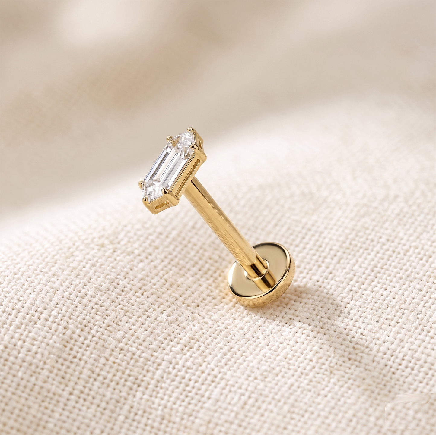 Gold stud earring with a clear gemstone on a beige fabric background