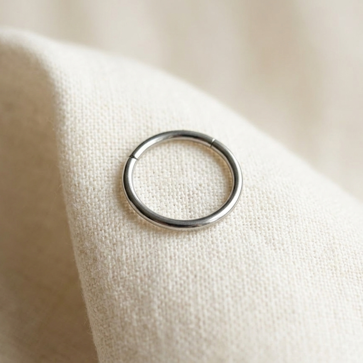 Silver titanium hinged hoop ring on cream linen fabric