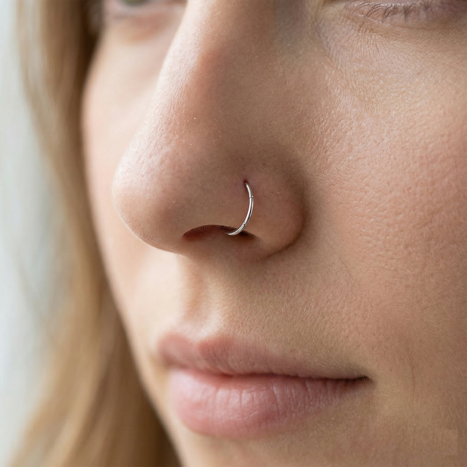 Silver nose hoop shown on nostril piercing