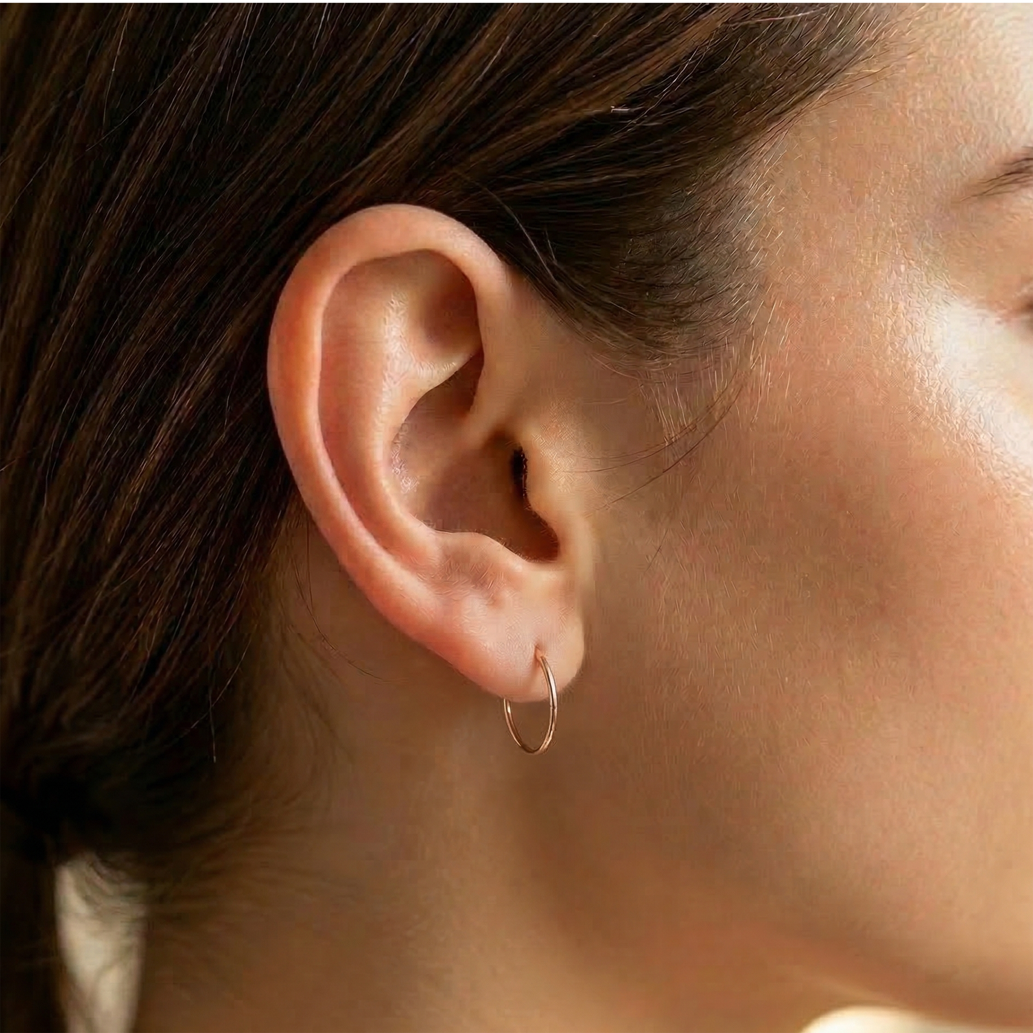 Rose gold hinged hoop shown on ear with piercings