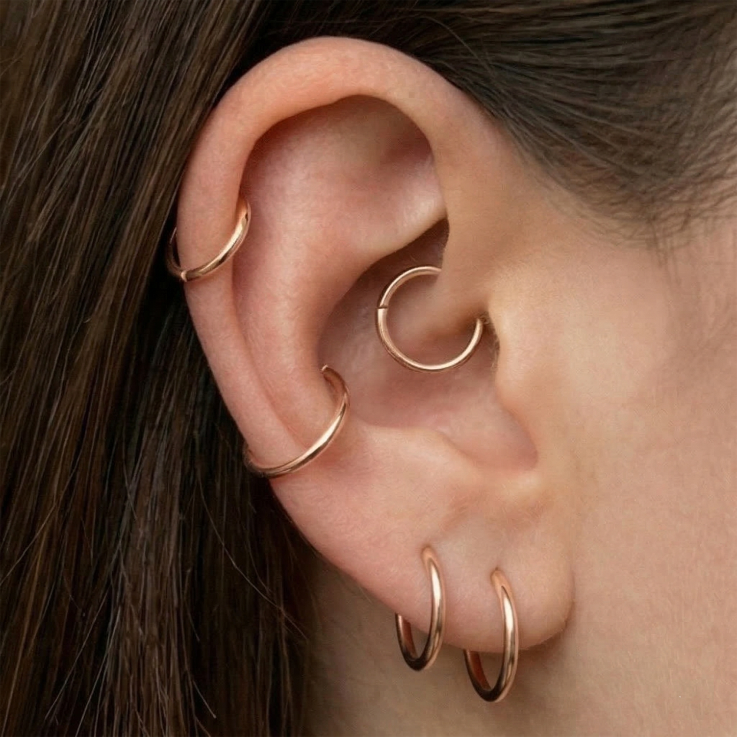 Rose gold hinged hoop shown on ear with multiple piercings