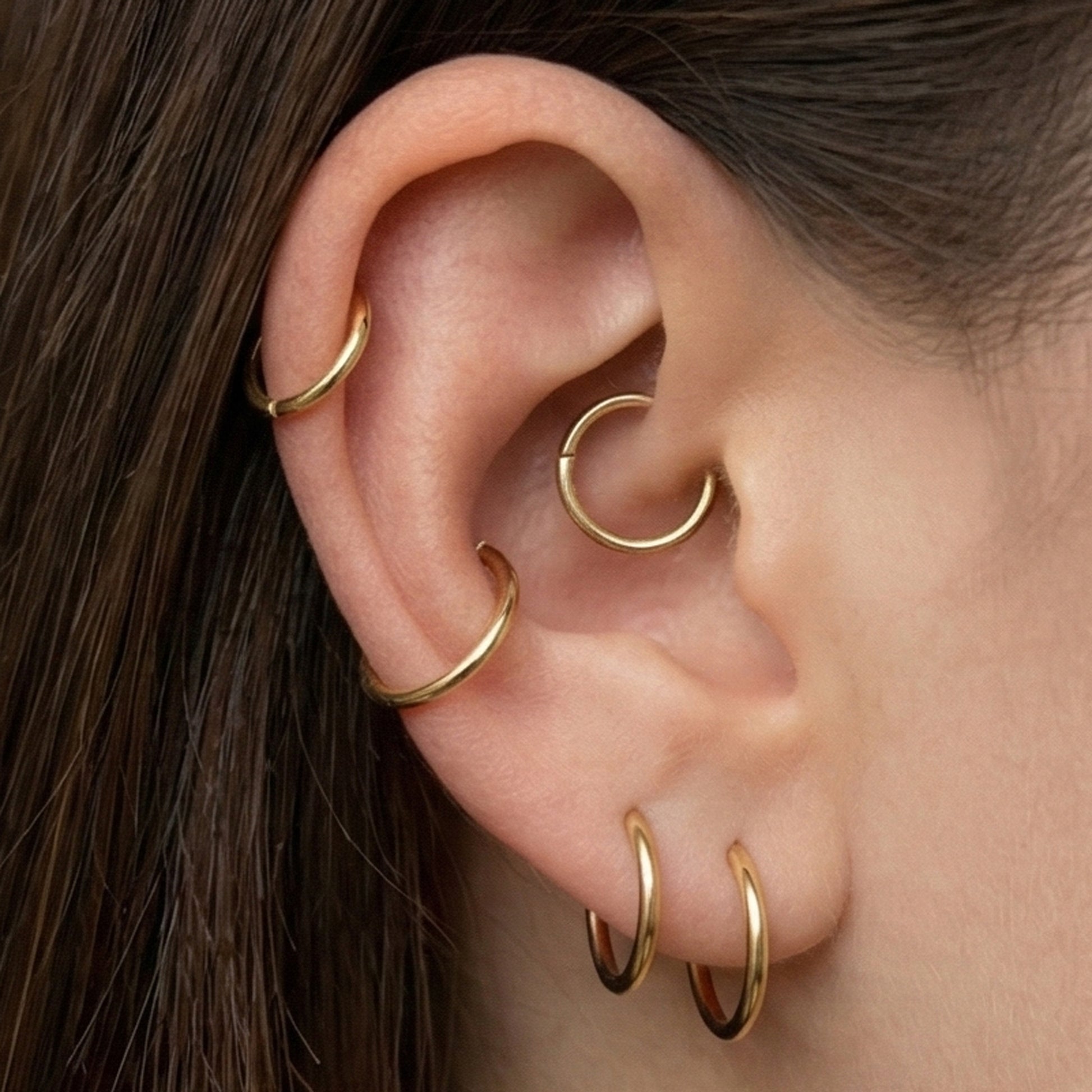 Gold titanium hinged hoop shown on ear with multiple piercings