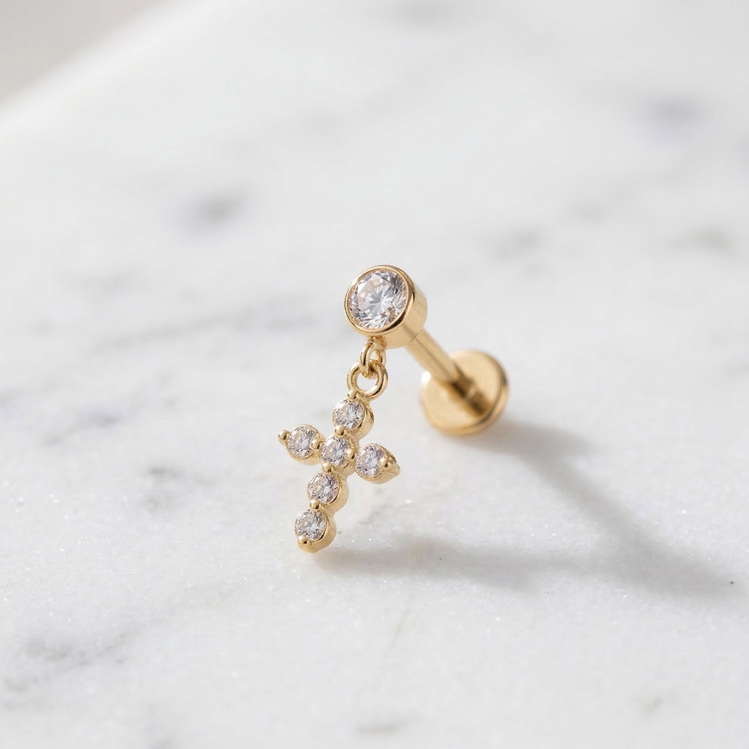 Gold titanium CZ cross dangle stud on marble surface
