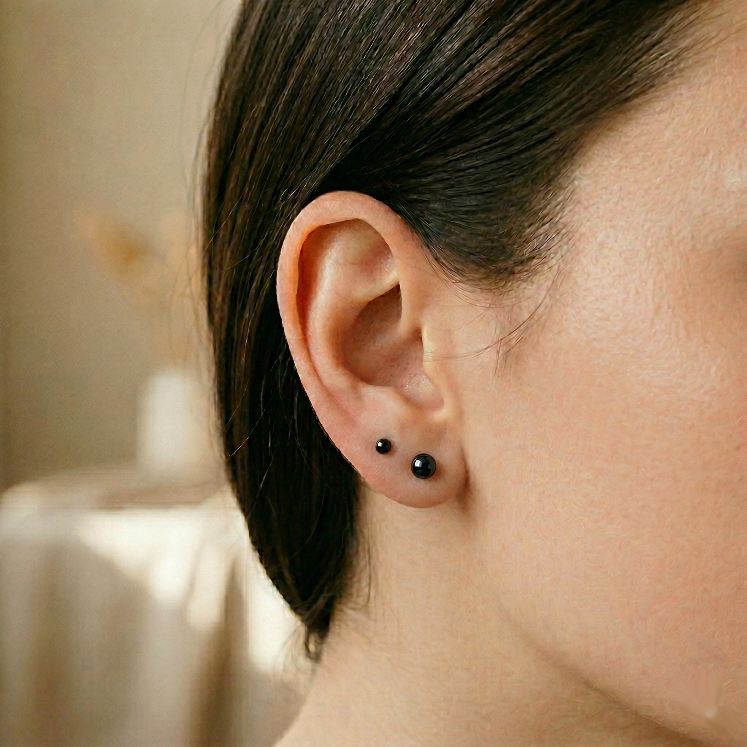 Black surgical steel ball stud earrings shown on ear with lobe piercing