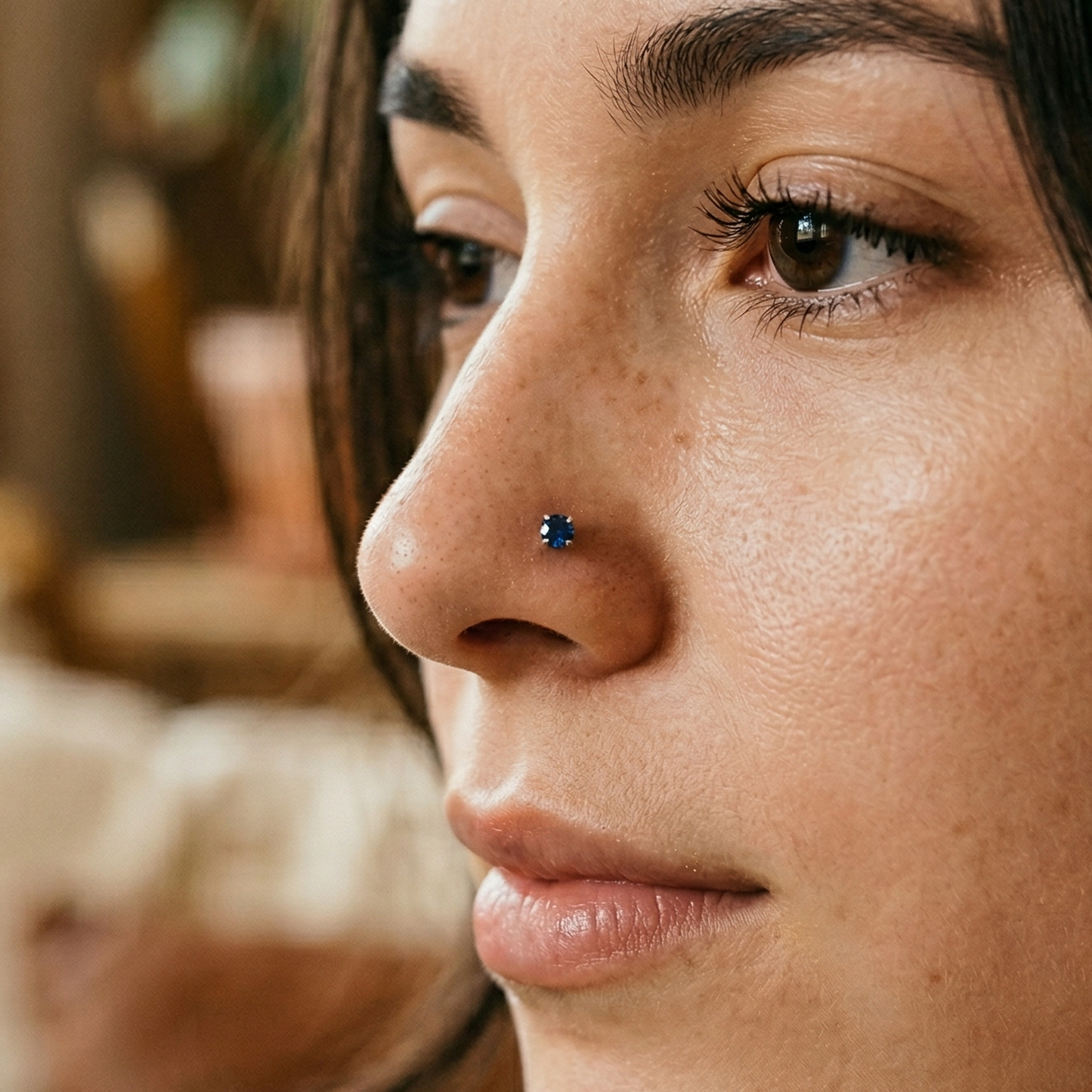 Titanium blue CZ prong stud shown on nostril piercing
