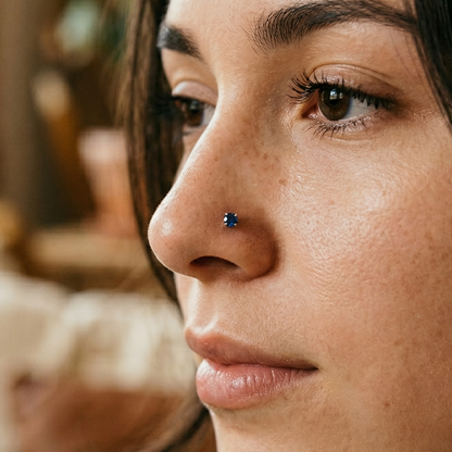 Titanium blue CZ prong stud shown on nostril piercing
