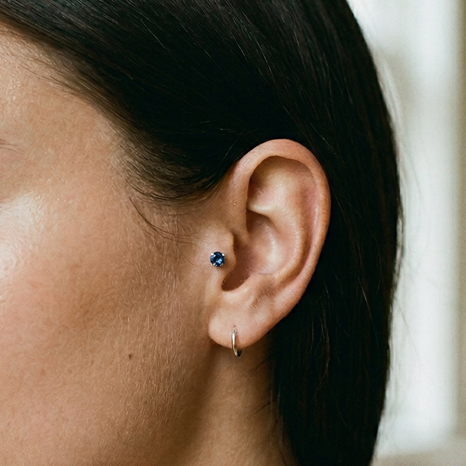 Titanium blue CZ prong stud shown on tragus piercing
