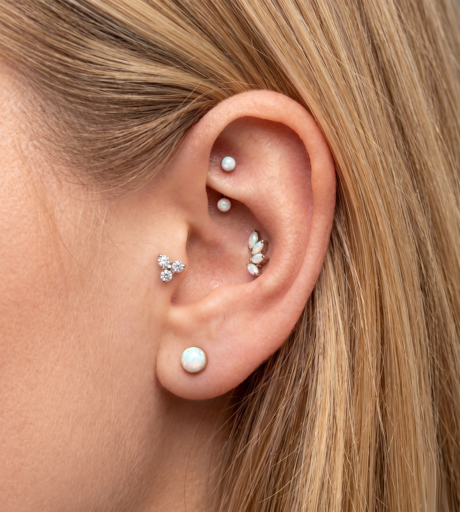 Close-up of an ear with multiple opal earrings on a blurred background