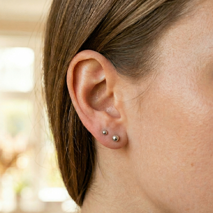 Silver surgical steel ball stud earrings shown on ear with lobe piercing
