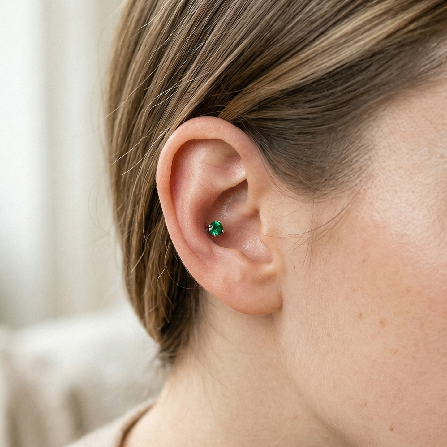 Titanium emerald green CZ prong stud shown on ear with conch piercing
