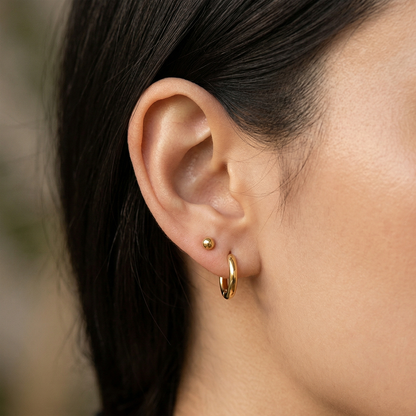 Gold titanium ball stud earrings close-up on ear with two lobe piercings