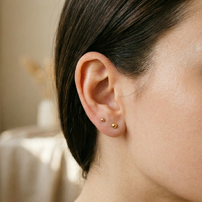 Gold titanium ball stud earrings shown on ear with double lobe piercings