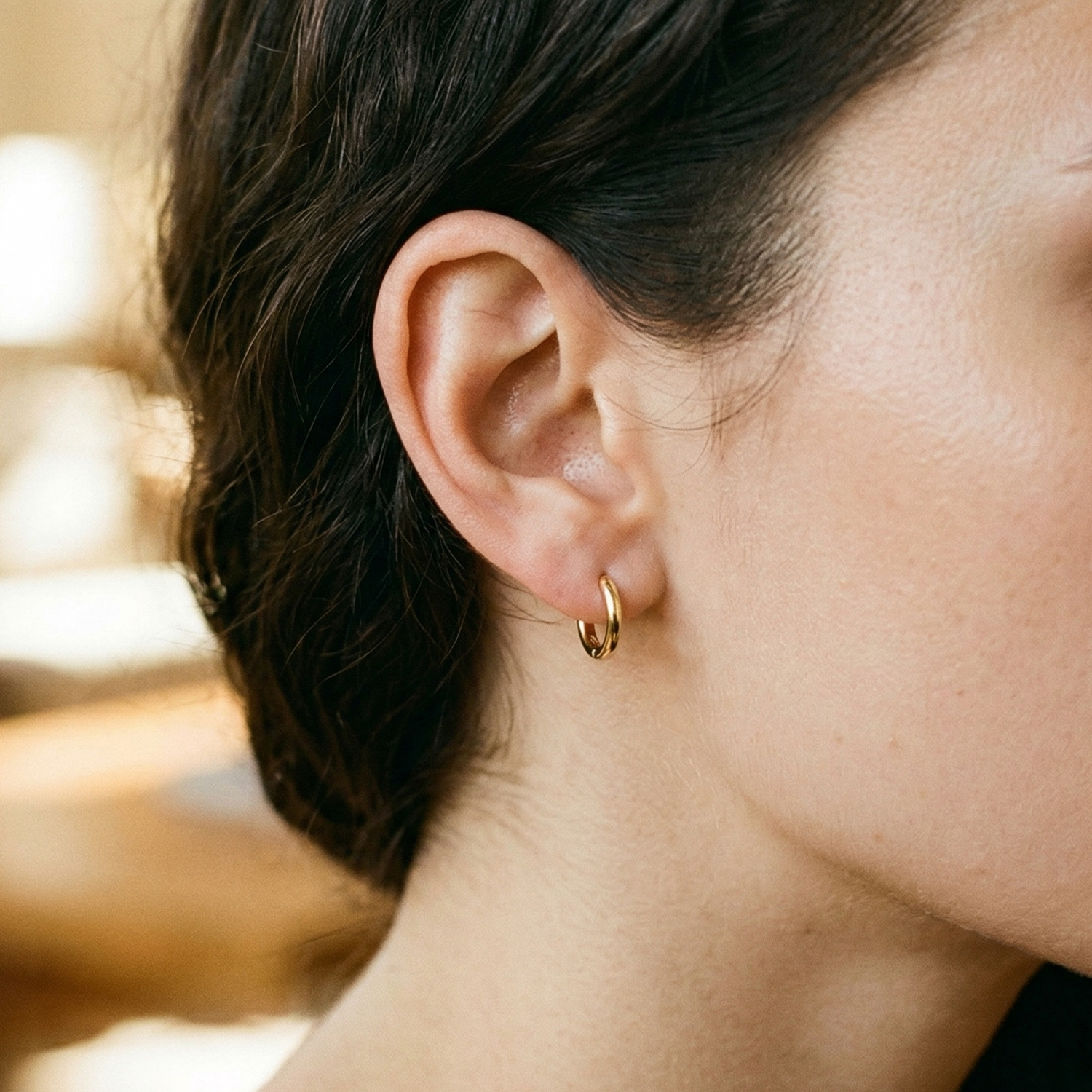 Gold titanium plain huggie hoop earrings shown on double lobe with CZ stud
