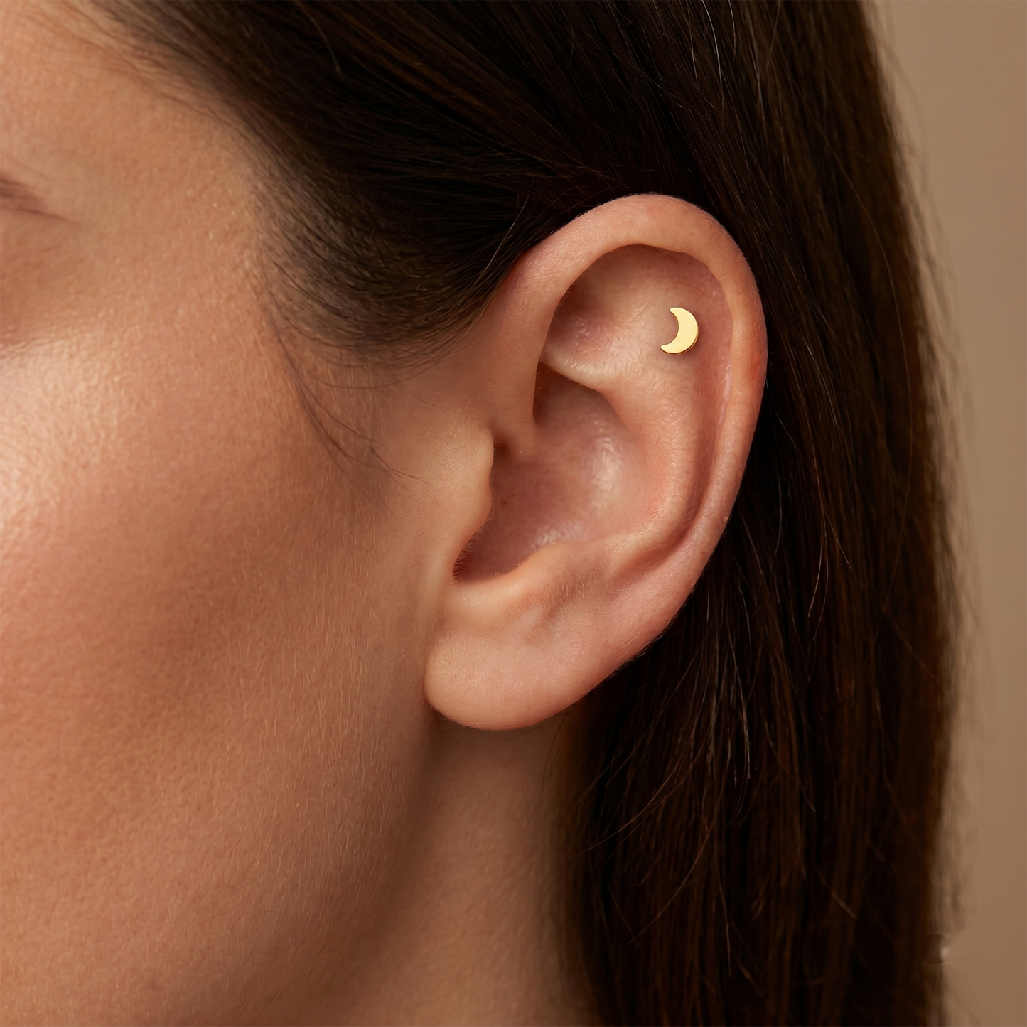 Close-up of an ear wearing a gold moon-shaped earring against a neutral background