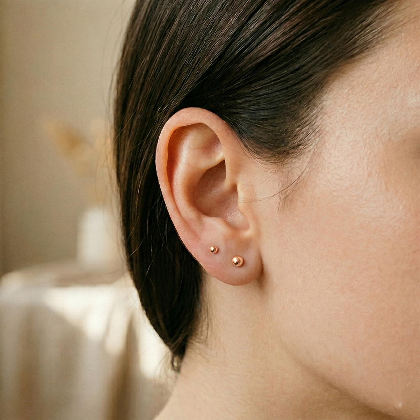 Rose gold surgical steel ball stud earrings shown on ear with lobe piercing